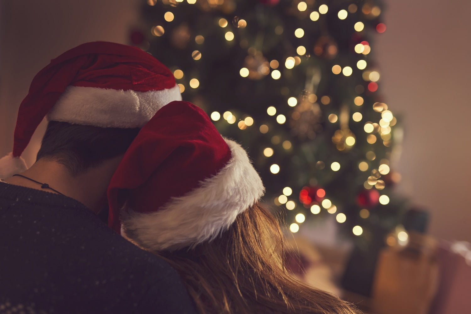 Couple in love sitting next to a Christmas tree, wearing Santa's hats,