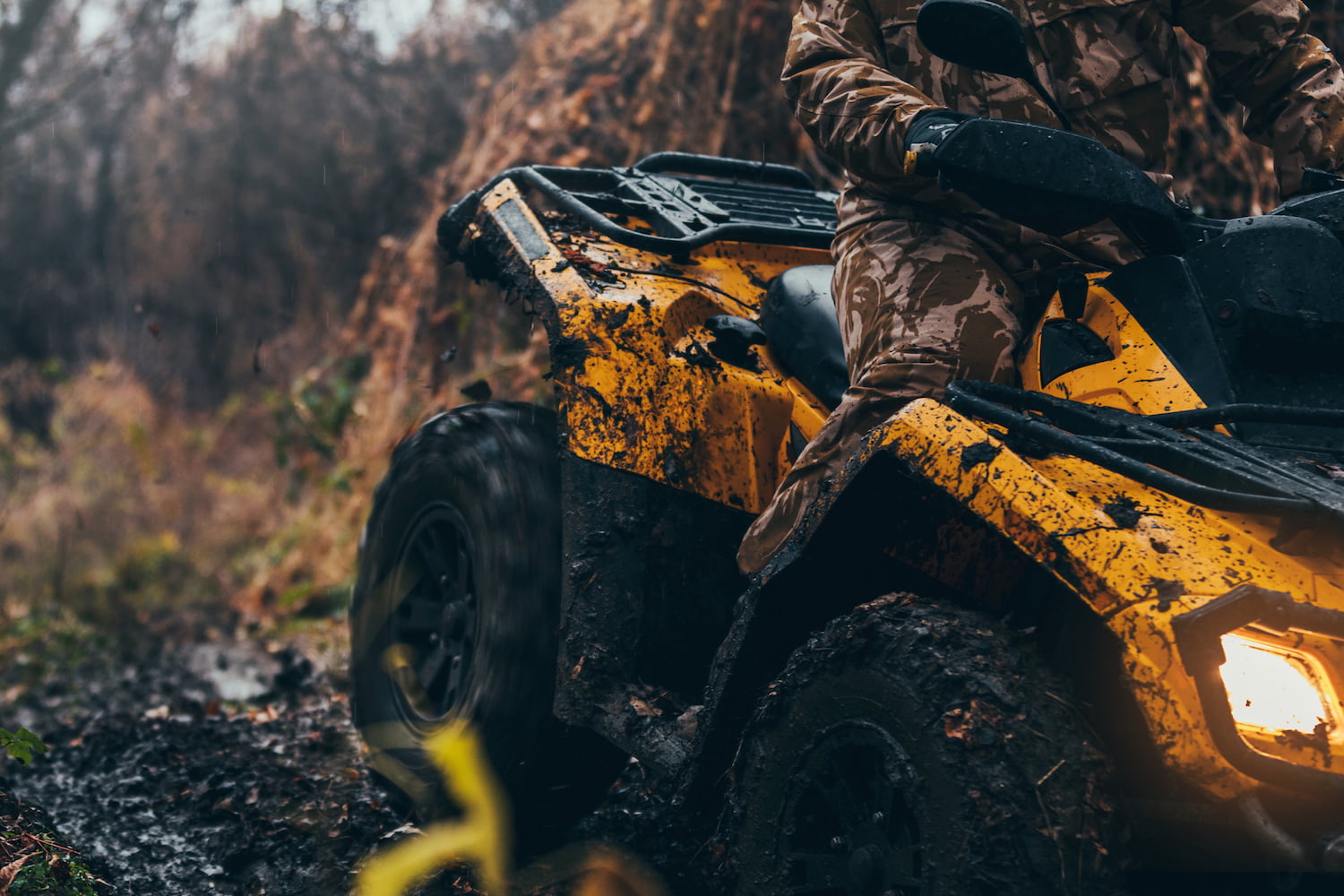 Man in camp riding on a muddy yellow ATV.