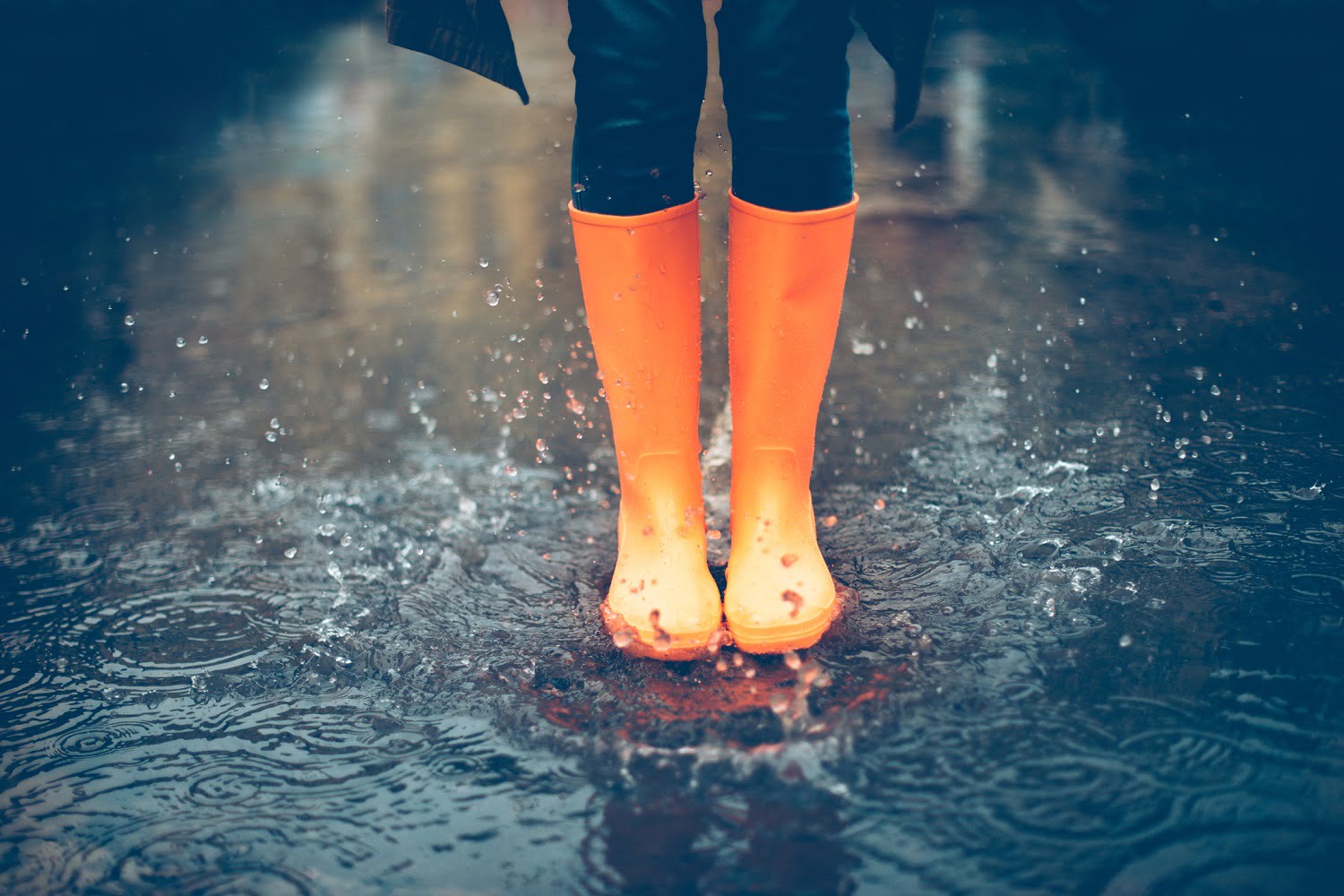 Close-up of woman in orange rubber boots jumping on a puddle