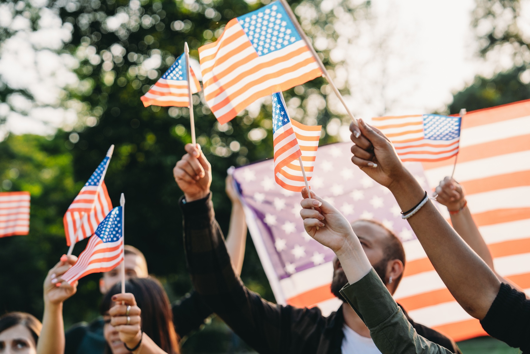 A group of people is waving small American flags at sunset. Concept for various topics like Happy Veterans Day, Labour Day, Independence Day.