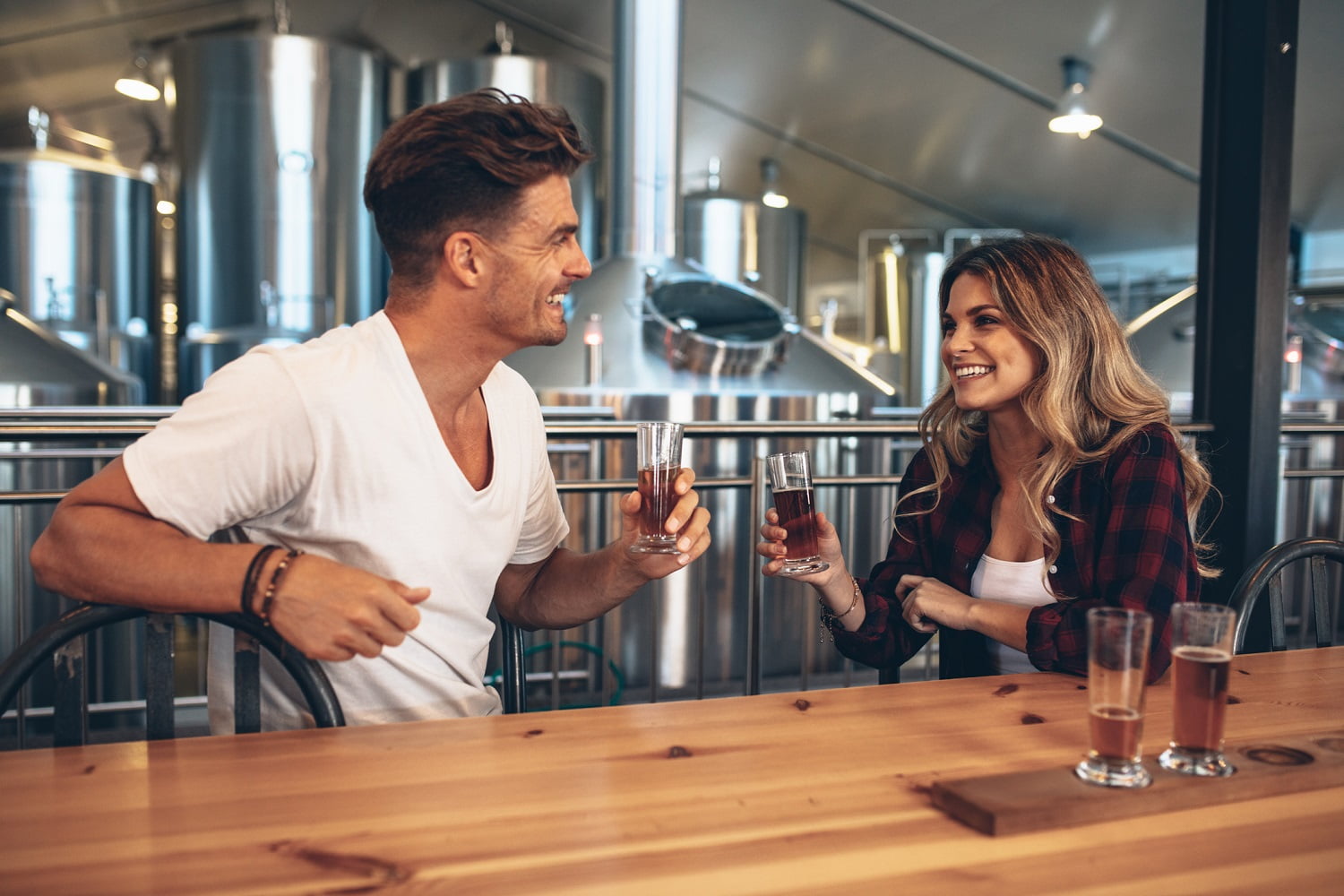 Couple at brewery toasting beers. Young man and woman tasting different varieties of craft beers.