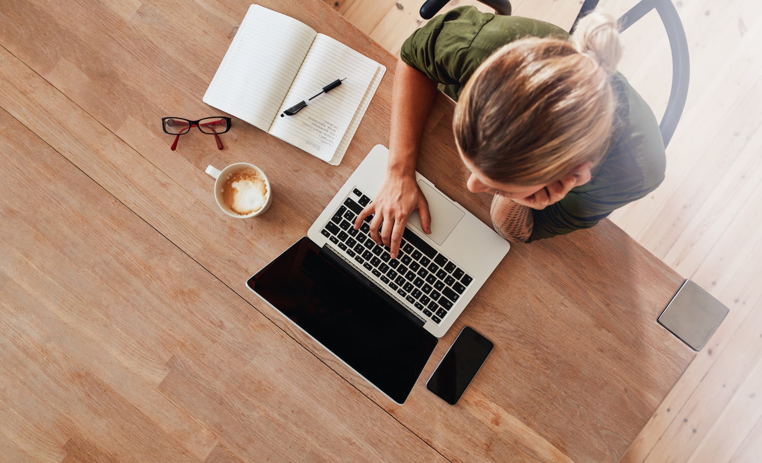 Top view of woman using laptop while sitting at cafe table with laptop, mobile phone, diary, coffee cup and glasses. Female surfing internet at coffee shop.