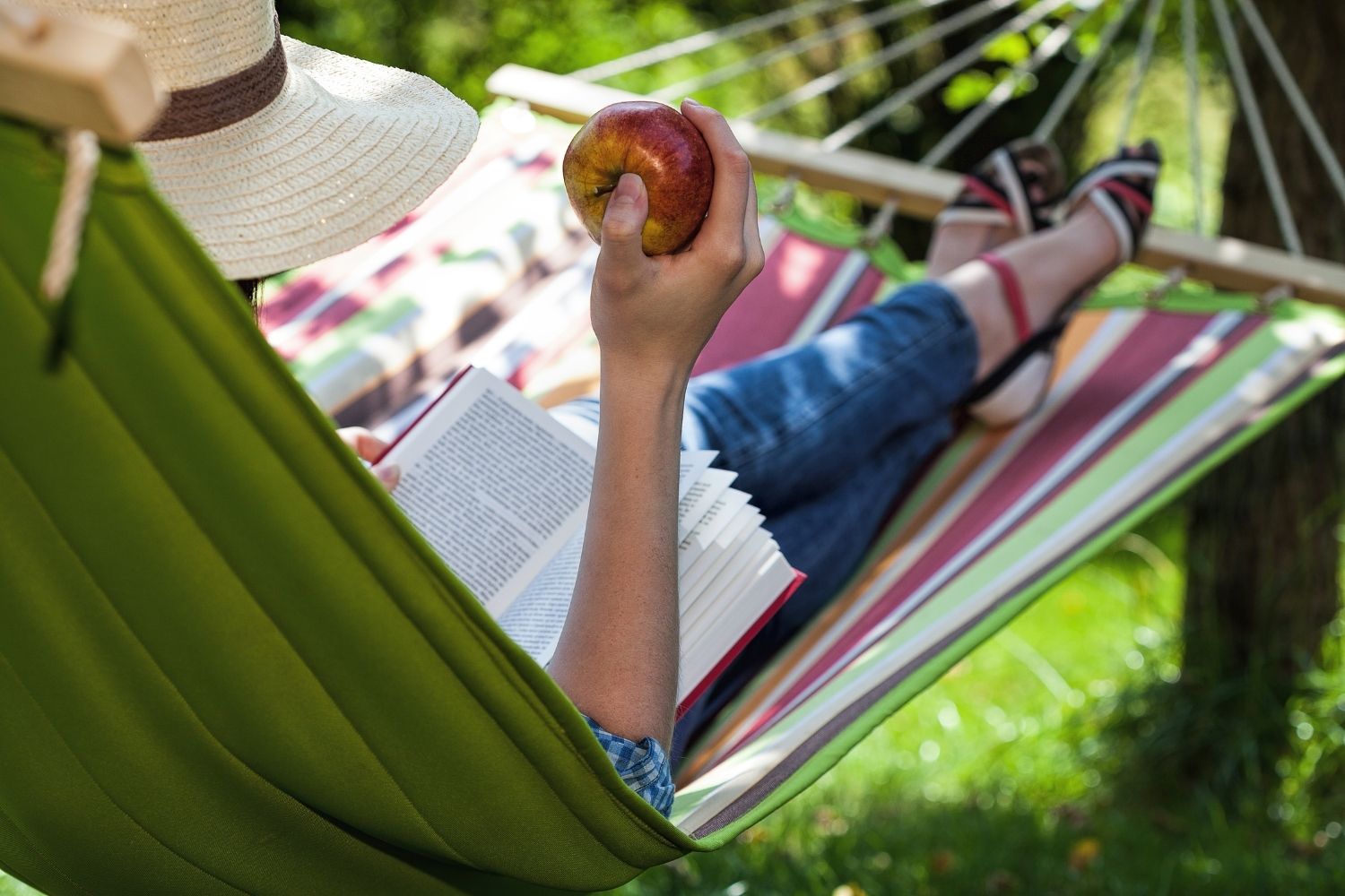 Lady reading a book in a hammock eating an apple.