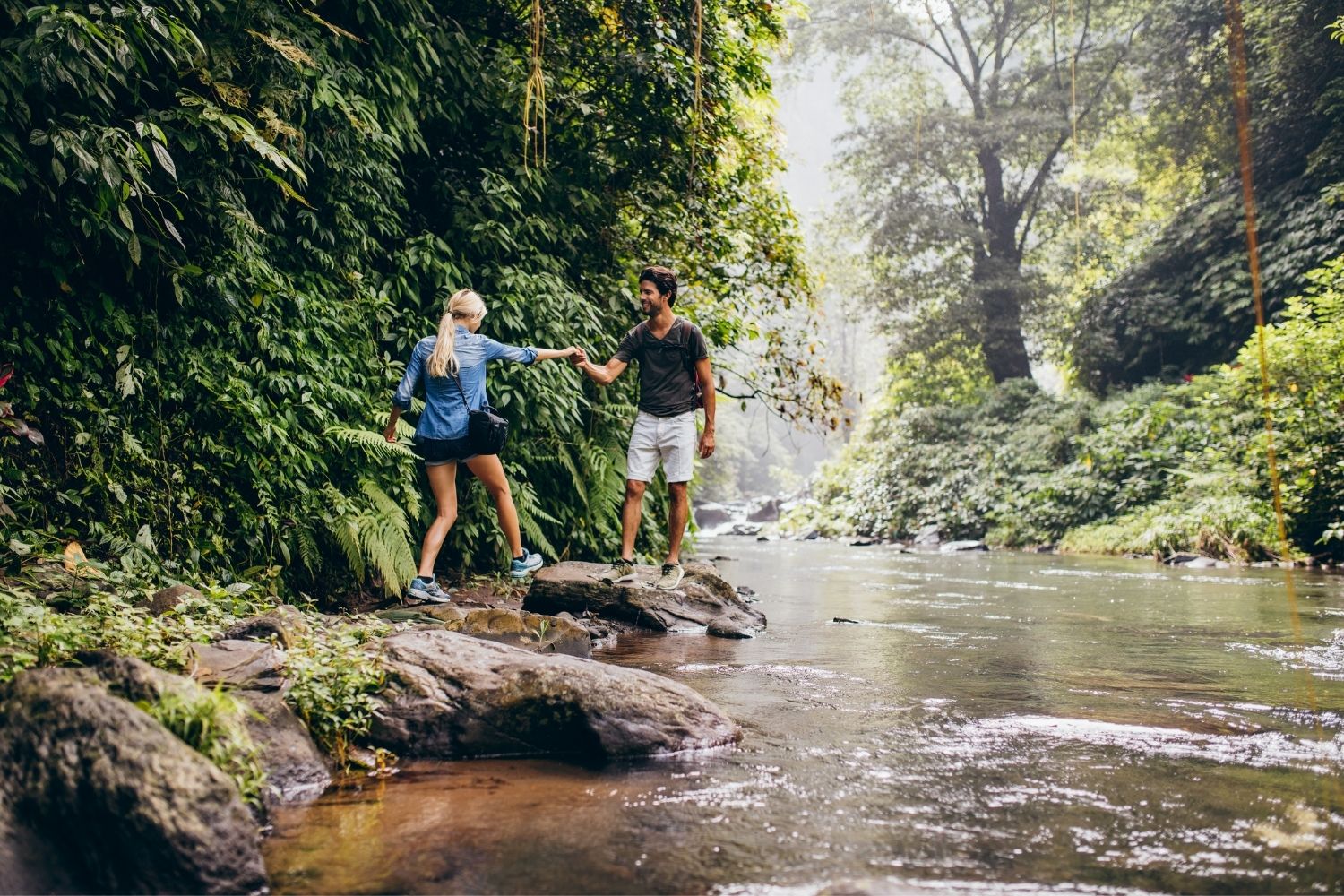 Couple hiking, one of our favorite things to do in the Hocking Hills, through the forest near a stream .