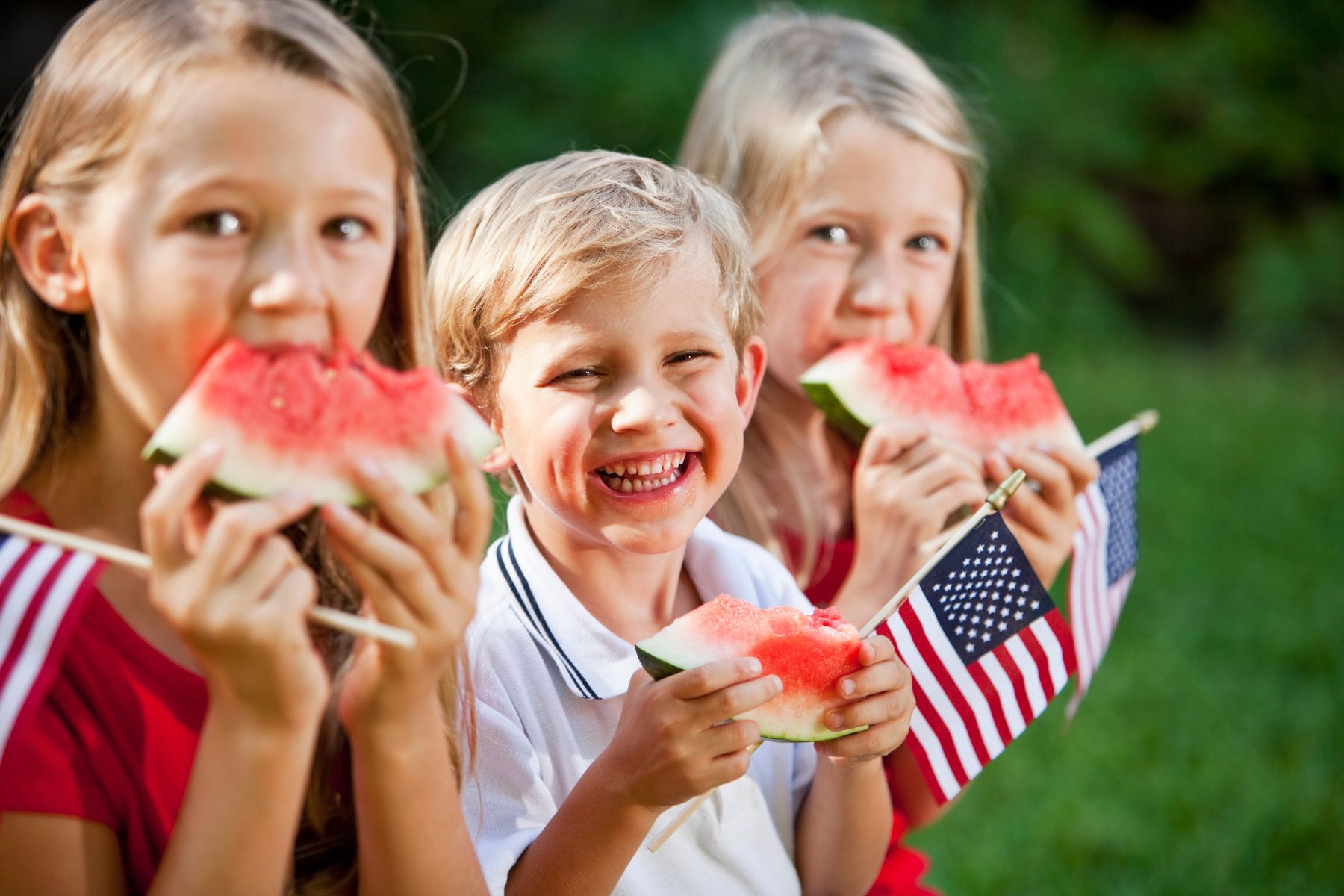 a group of children eating watermelon and holding American flags during their Memorial Day trip to the Hocking Hills